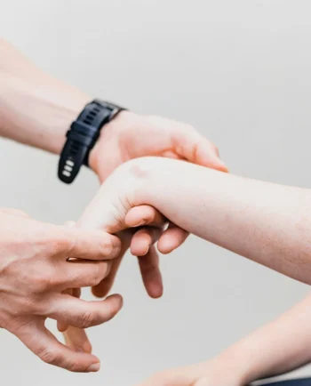 Ein Physiotherapeut führt in der Praxis Schulze-Bramey Physiotherapie eine Handgelenk-Untersuchung durch. Der Therapeut mit einem schwarzen Sportarmband hält und überprüft sorgfältig das Handgelenk einer Patientin mit sichtbaren Sommersprossen.