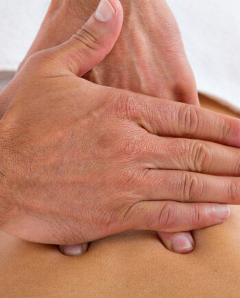 Detailaufnahme einer Osteopathie-Behandlung, bei der ein Therapeut mit gezieltem Druck seine Hände auf den unteren Rückenbereich eines Patienten legt, um Verspannungen zu lösen und die Beweglichkeit zu verbessern.