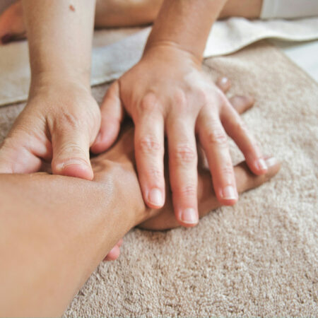 Eine Nahaufnahme zeigt die Hände einer Masseurin, die eine klassische Massage an einem Patienten durchführt. Die sanften, gezielten Grifftechniken auf dem Rücken des Patienten, der auf einer gemütlichen Liege entspannt, fördern die Entspannung und Durchblutung.